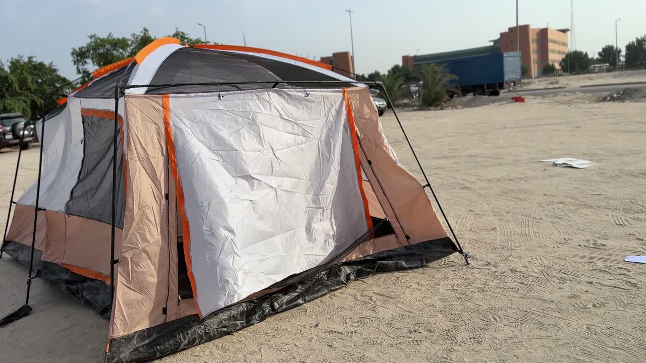 A camping tent being assembled in a desert area, showing the structure partially built with poles and fabric. Clear daylight, outdoor adventure vibe, useful for travel, camping, survival, tourism