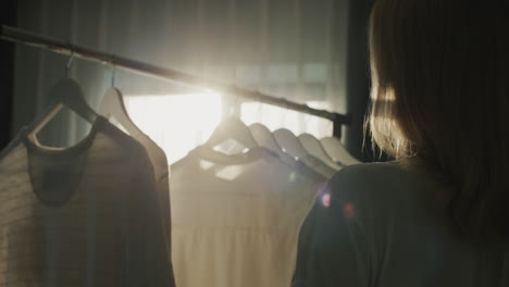 a cute woman hangs clothes on a rack, her silhouette beautifully illuminates the sun from the window