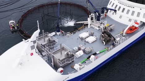 advancing drone shot of a well boat delivering fish to a fish farming pen