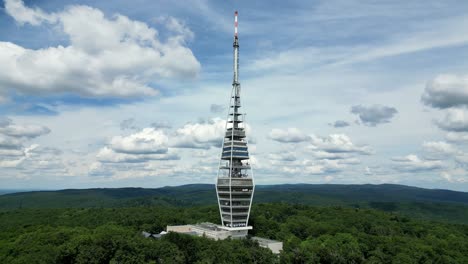 wide drone orbit of kamzik tower surrounded by forested hills in bratislava, slovakia, blue sky view