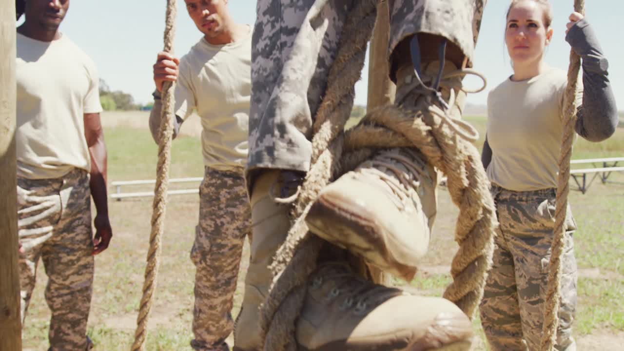grupo diverso viendo soldado masculino en uniforme subiendo la cuerda en el curso de obstáculos del ejército en el sol