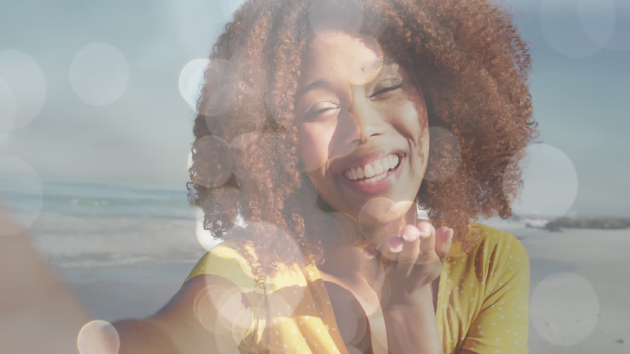 Animation of bokeh over happy biracial woman sending kisses