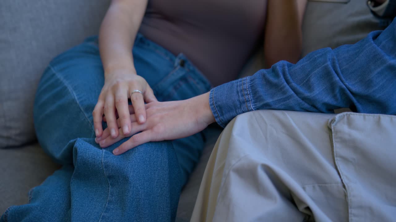 Asian and African American women on patio holding mugs, left speaking right reaching, comforting