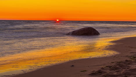 5K-Time-lapse-shot-of-red-colored-sun-going-down-at-horizon-behind-wavy-ocean-with-swimming-people