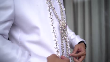 a groom in a necklace and a white coat