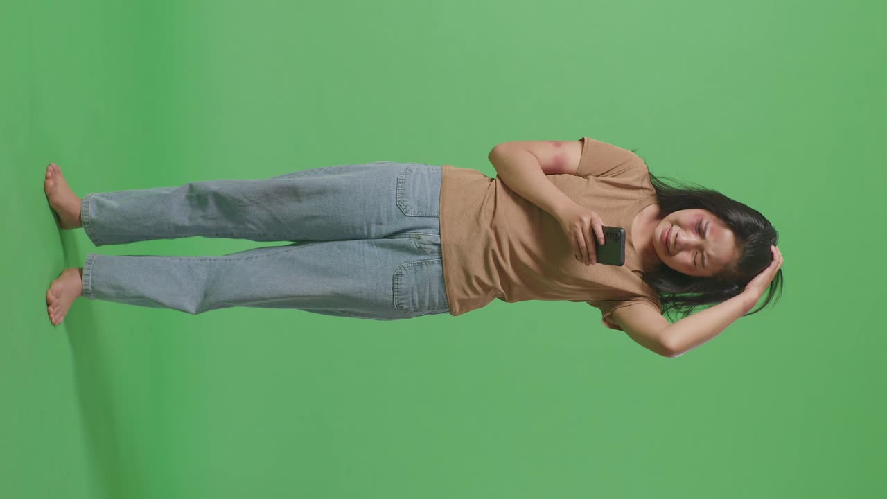 얼굴과 팔에 이 묻은 젊은 아시아 여성의 몸은 스마트폰을 보고 녹색 화면 배경 스튜디오에서 울고 있습니다.