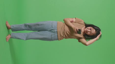 cuerpo lleno de joven mujer asiática víctima de violencia con moretones en la cara y los brazos mirando el teléfono inteligente y llorando en el estudio de fondo de pantalla verde