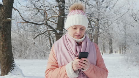 Eine-Frau-In-Einer-Rosa-Jacke-Genießt-Einen-Spaziergang-In-Einem-Winterpark-Benutzt-Ein-Handy-4k-Zeitlupenvideo