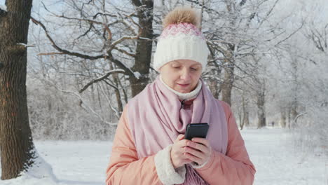una mujer con una chaqueta rosa disfruta de un paseo en un parque de invierno usa un video en cámara lenta de 4k de teléfono móvil