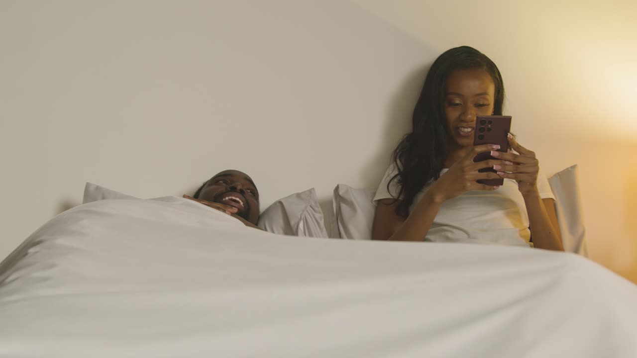 pareja en casa por la noche acostada en la cama con una mujer mirando el teléfono móvil 1