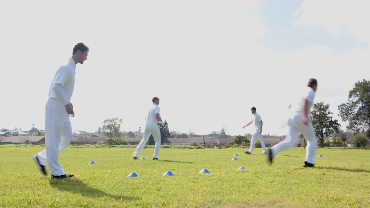 Team of multiracial male cricket players practicing cricket wearing cricket whites on pitch
