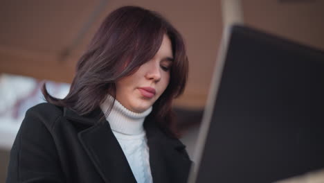 student focused on her laptop, studying or working intently in outdoor patio space, blurred background features a building and soft lighting