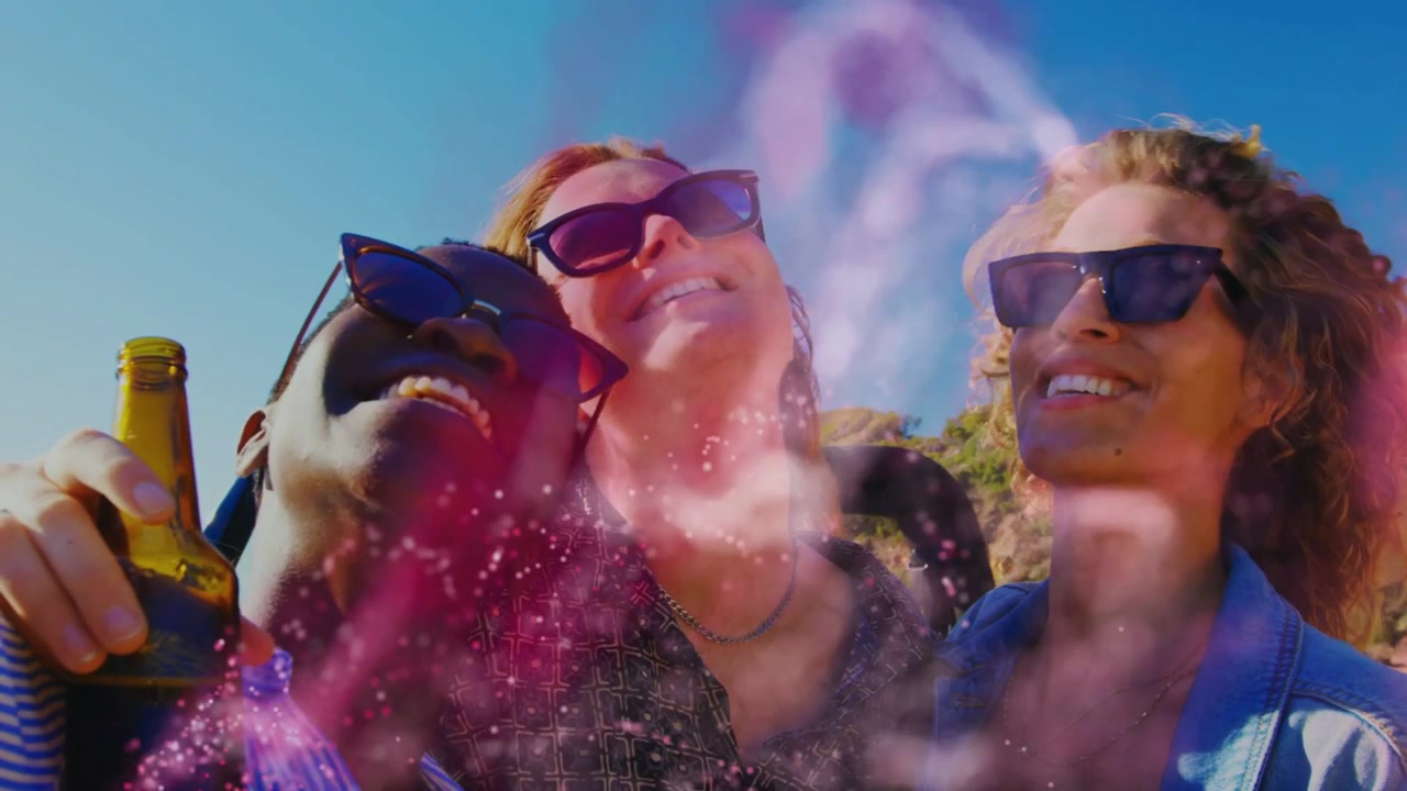 Tre donne che si appoggiano e ridono, tenendo una bottiglia, con una sovrapposizione rosa che svanisce rivelando occhiali da sole, celebrando un viaggio
