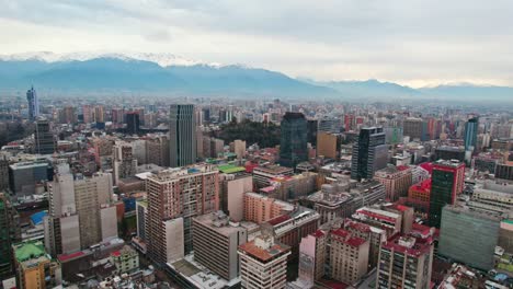 Dolly-Para-Establecer-Una-Vista-Aérea-Del-Centro-De-Santiago-De-Chile-Con-Edificios-Residenciales-Y-Gubernamentales-Con-El-Cerro-Santa-Lucía-En-El-Centro-Y-La-Nublada-Cordillera-De-Los-Andes-Al-Fondo.