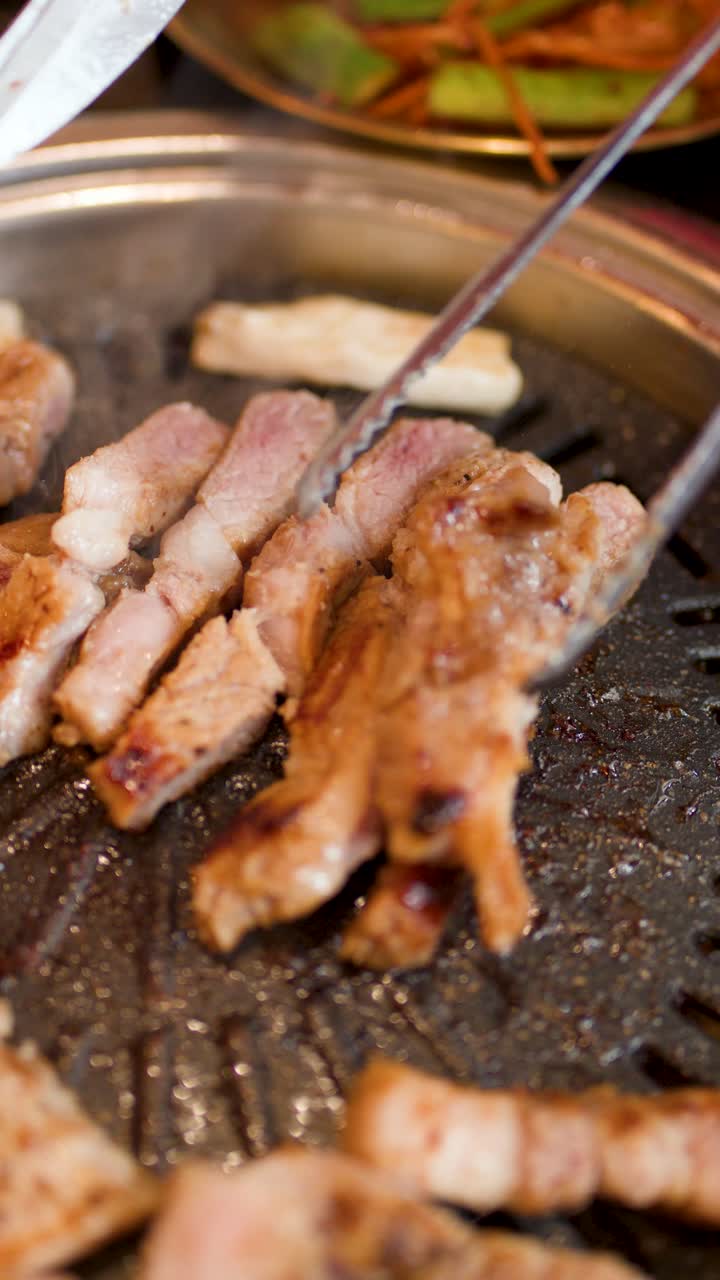 Penjepit menata irisan daging babi bagian perut di atas panggangan barbekyu Korea yang panas, pandangan dari atas