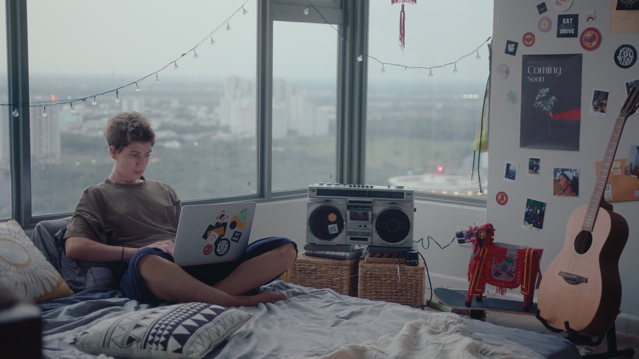 Young Woman Sitting on Bed and Using Laptop at Home