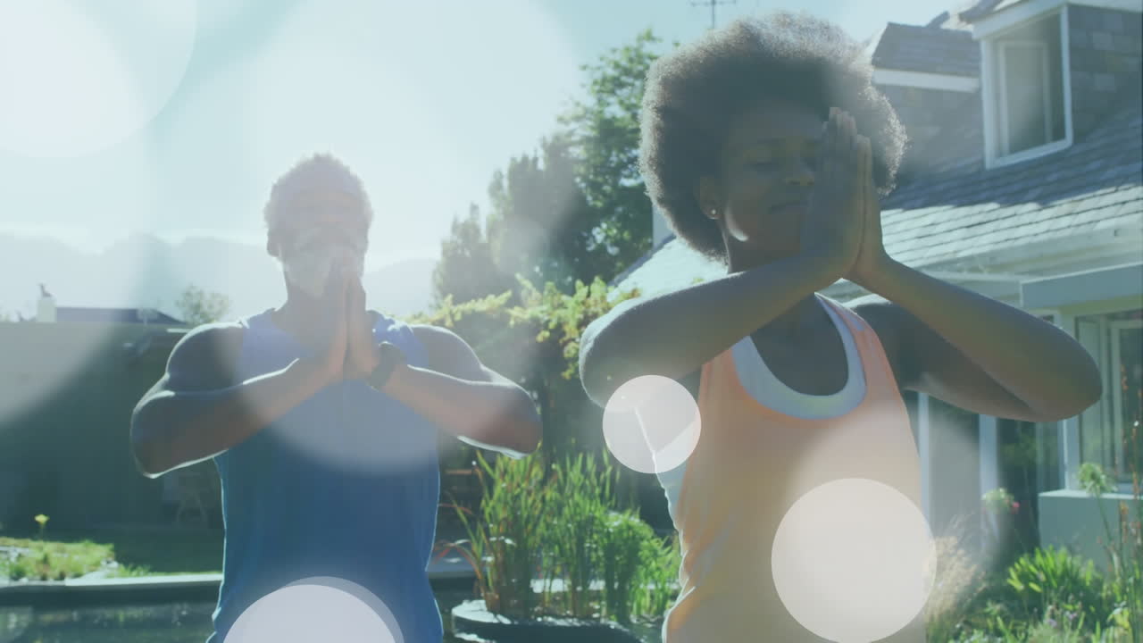 Animation of light spots over african american couple doing yoga, meditating, slow motion