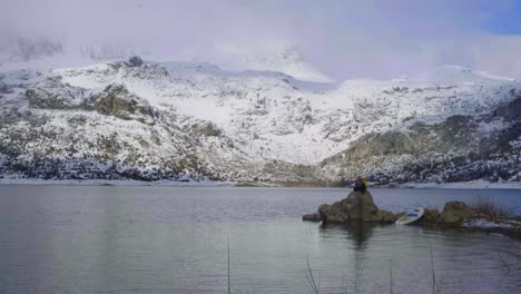 Man-near-paddle-board-on-shore-near-water-and-mountains-on-coast