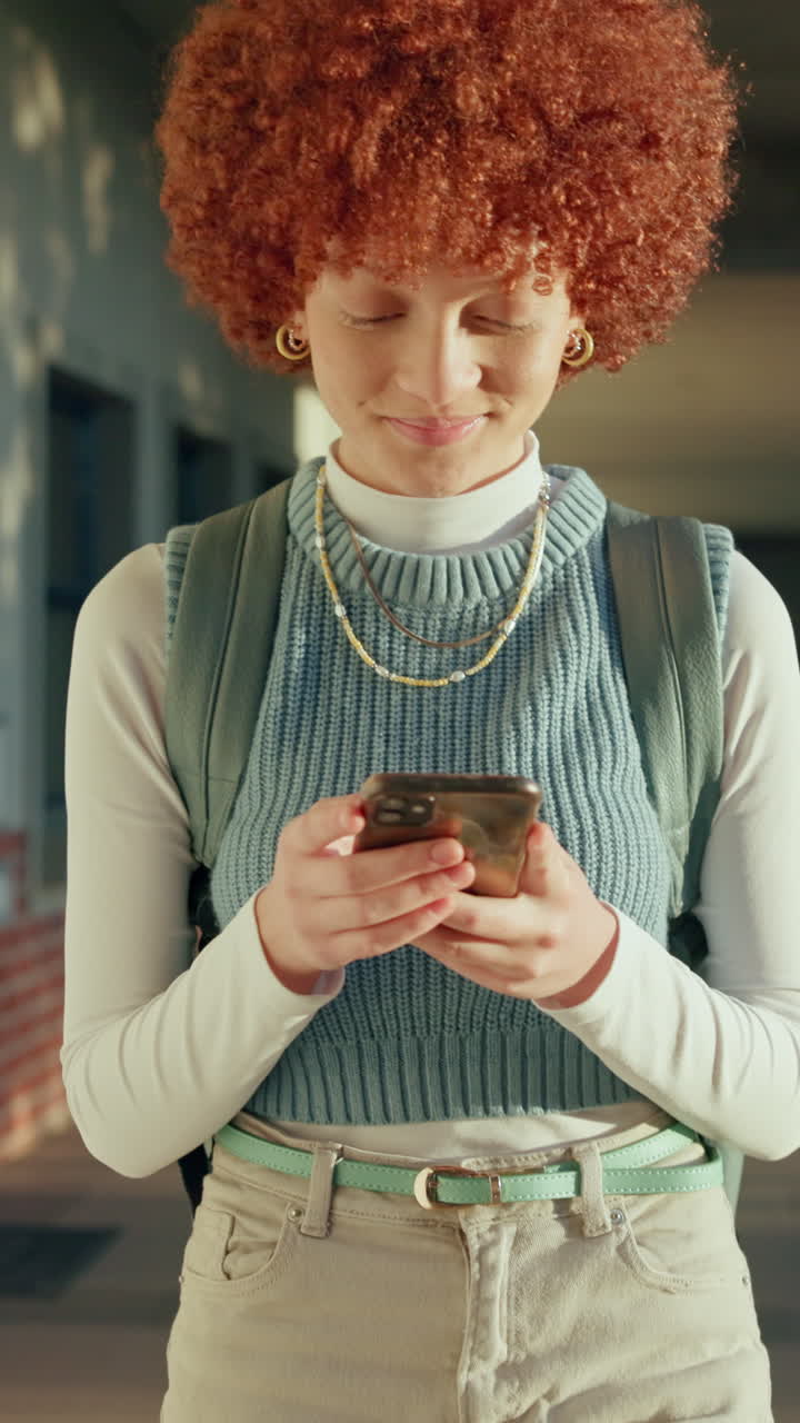 Giovane donna con capelli rossi ricci che scrive messaggi sullo smartphone.