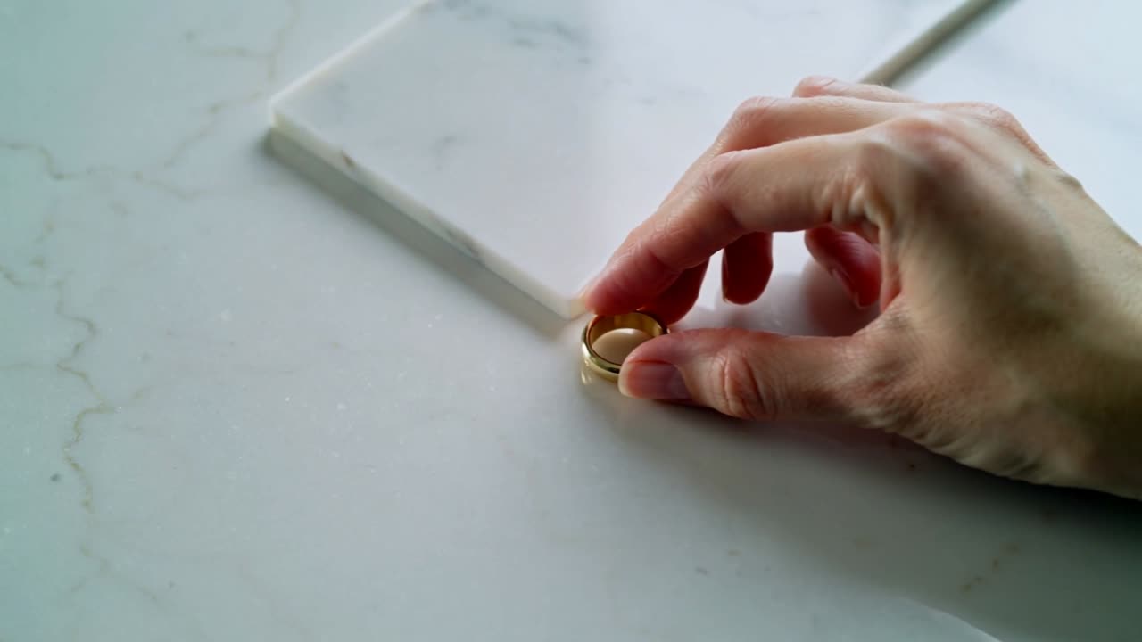 Mano destra che entra nell'inquadratura e allinea anelli d'oro sul bancone, preparando uno scatto di prodotto di gioielli.