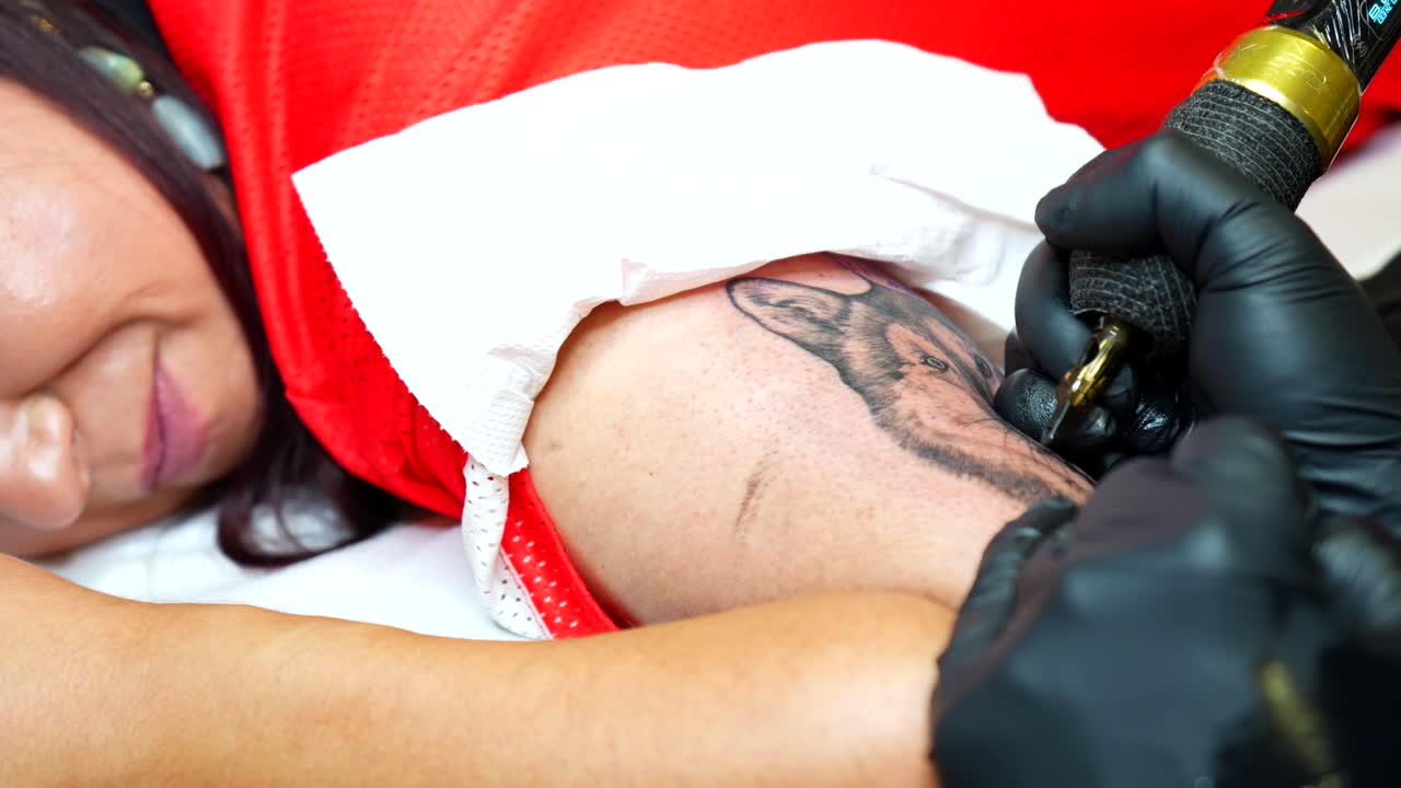 Close-up view of a woman getting a realistic wolf tattoo on her upper arm