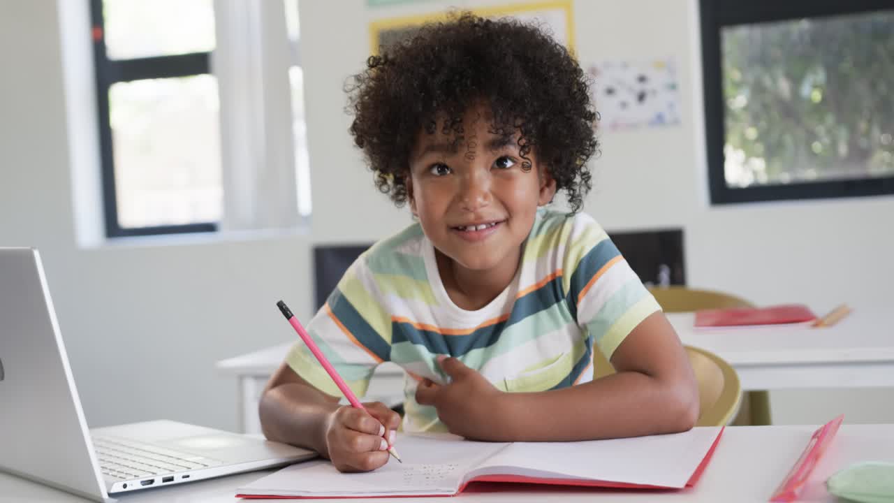 Giovane afroamericano che studia alla scrivania, scrive con una matita rosa su un quaderno rosso, si ferma per sorridere