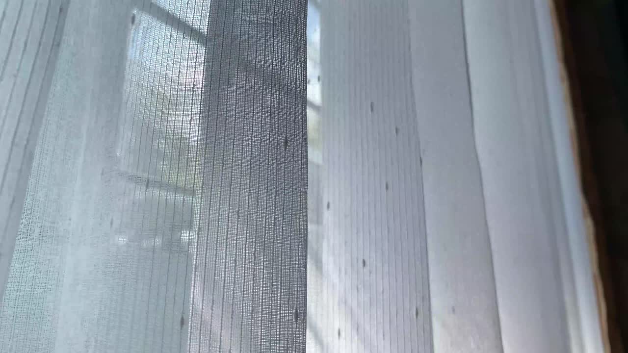 The white curtains on the windows of the house move in the wind in the afternoon