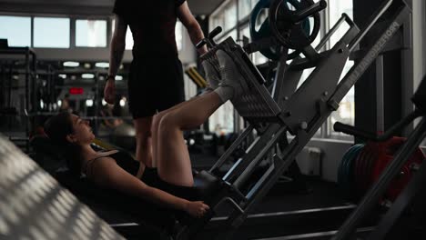 woman doing leg press exercise in the gym with personal trainer