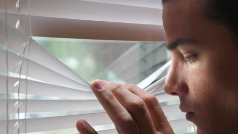 young man looking out the window through the blinds