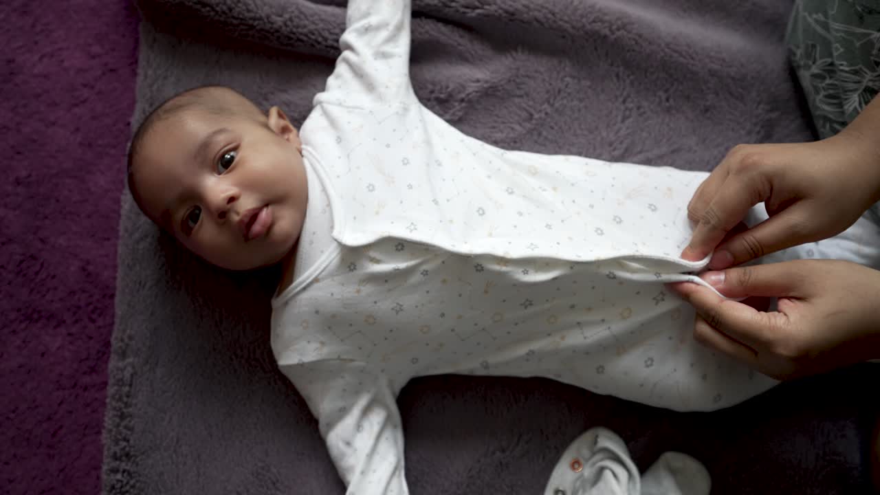 madre abrochándose el camisón de su hijo de 2 meses mientras él se acuesta en una manta