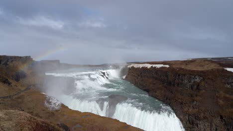 majestic gullfoss waterfall with vibrant rainbow in iceland, cloudy skies overhead, winter season