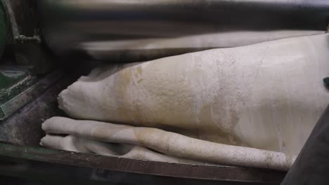 mid shot of rubber material being rolled and processed through heavy duty machinery in factory