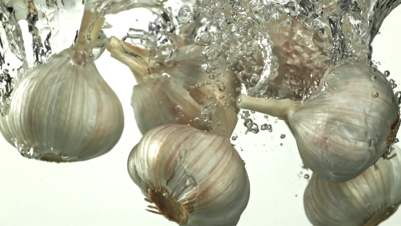 Bulbi d'aglio freschi che cadono nell'acqua al rallentatore