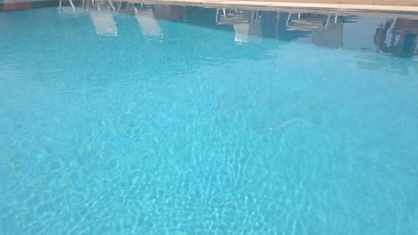 fading out tilt shot of sun loungers - umbrellas adjacent to luxury pool on sunny day with blue sky with mountains in background