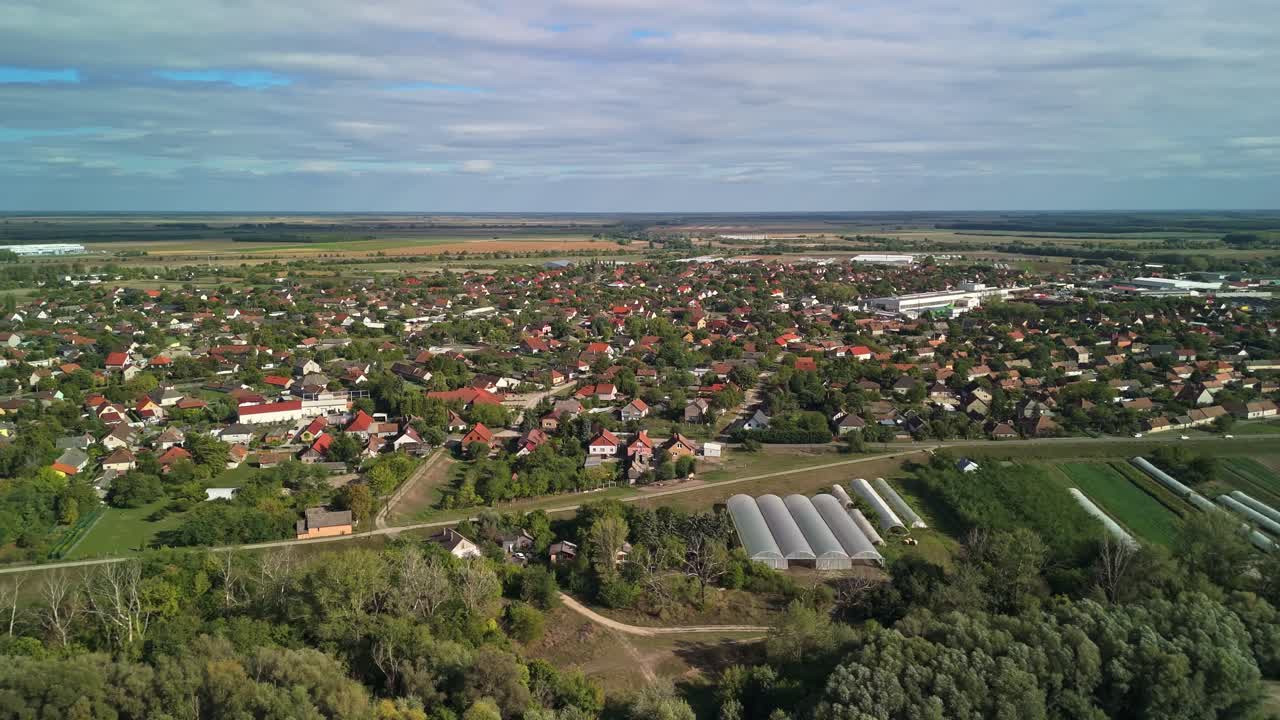 Drone video moving sideways over Dunavecse, Hungary, showing the small-town houses, cultivated fields and greenhouses surrounded by lush greenery on a sunny day