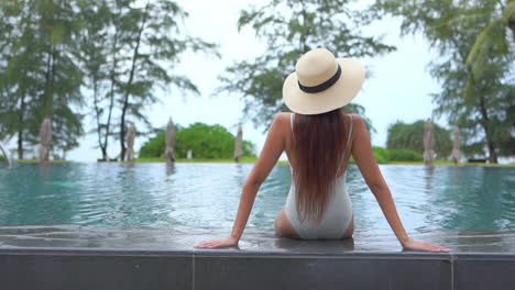 rear shot slim, fit woman on holiday sitting on swimming pool border