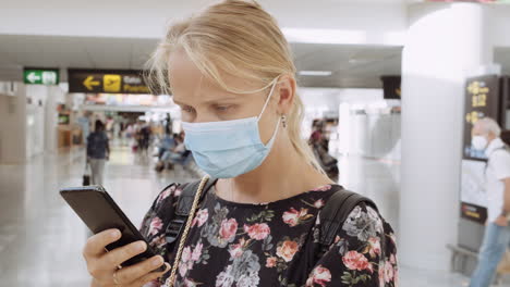 Sie-überprüft-Nachrichten-Vor-Der-Flugfrau-Mit-Maske-Und-Handy-Am-Flughafen