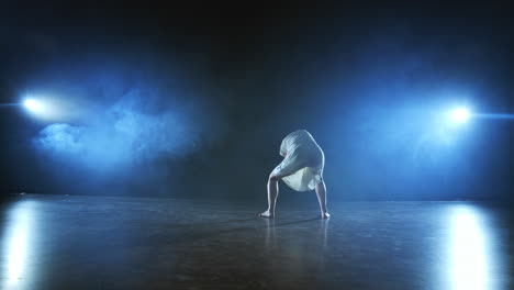 bailarina moderna en un vestido corto blanco realiza plásticos hermosos bailes dramáticos corriendo a través del escenario cayendo al suelo y girando. linternas y humo.