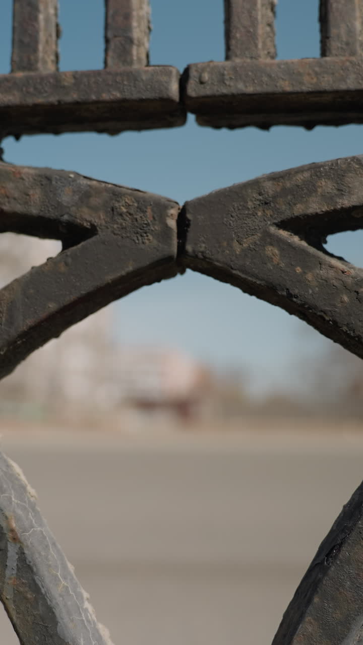 Close view of a weathered metal fence with intricate patterns, highlighting the texture and wear of the metal, with cars passing by