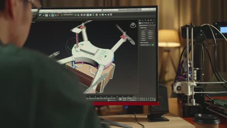 over the shoulder asian engineer working on personal computer and 3d printer, screen shows cad software with 3d prototype of drone delivery