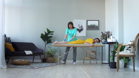 Two-girls-in-a-beauty-salon-master-in-a-Bathrobe-and-gloves-doing-the-procedure-to-remove-hair-on-the-legs-with-a-sugar-mixture