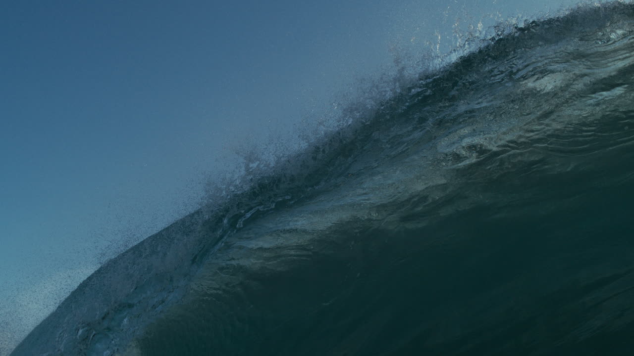 Tube wave surges forward in clean clear ocean, sunlight shimmering on surface, extreme slow motion