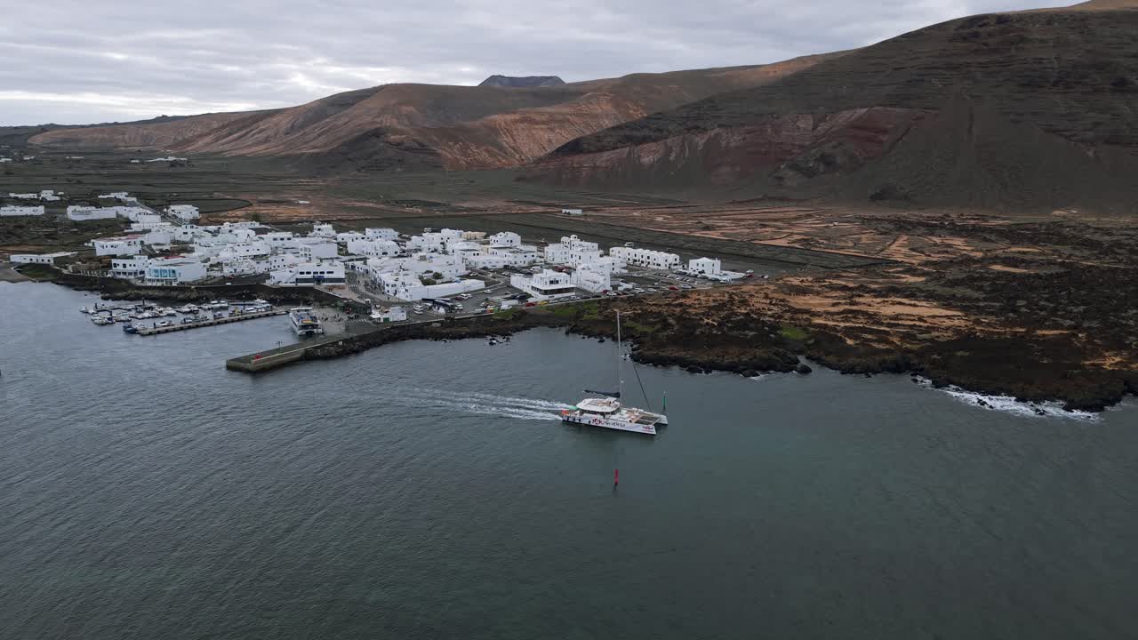 Luftaufnahme von Orzola, Lanzarote: Weiße Gebäude, Hafen, Fähre und Vulkanlandschaft unter bewölktem Himmel. Kanarische Inseln Tourismus und Reiseziel Fotografie