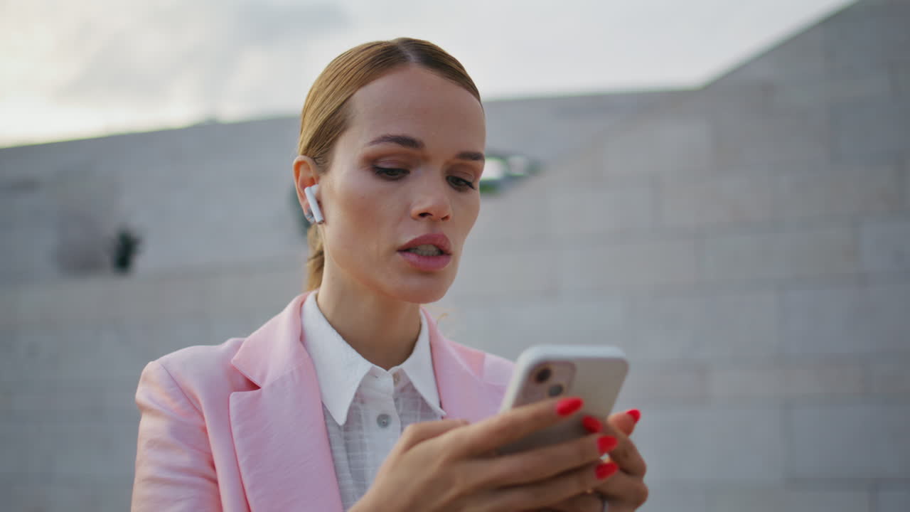 Primo piano di un manager impegnato che scorre lo smartphone e fa una chiamata con gli auricolari per strada.