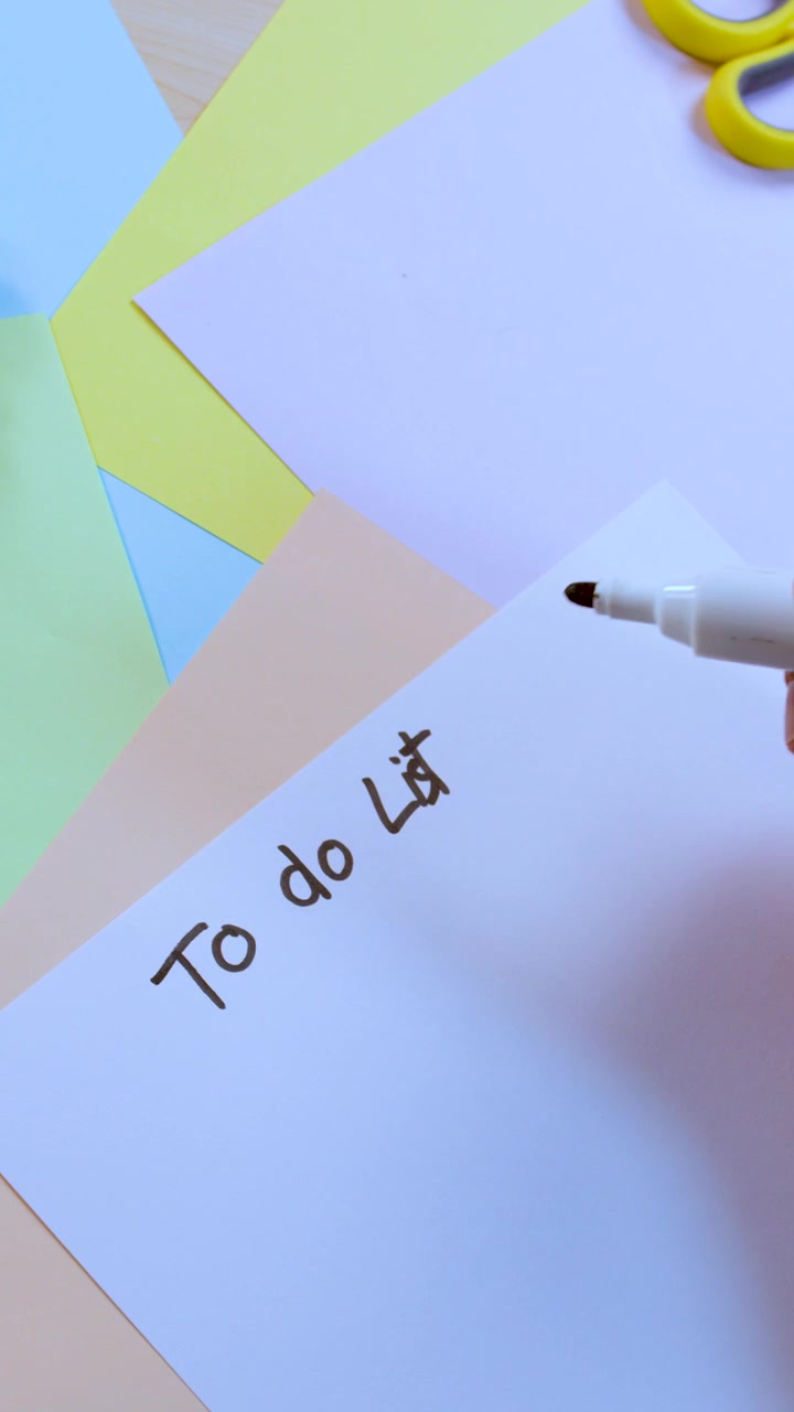 Una persona scrive 'Lista delle cose da fare' su carta bianca con un pennarello, vista dall'alto, illuminazione brillante.