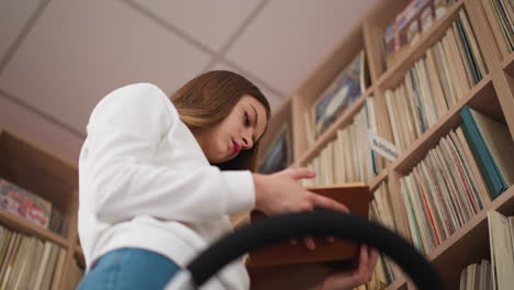 lady learns book pages taken from top shelf standing on ladder. constant female visitor of bookstore browsing novel before buying. lady reader holds book