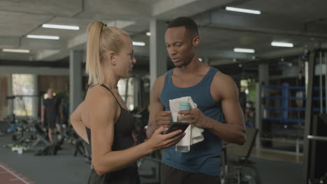 caucasian female monitor and an athletic african american man talking in the gym.