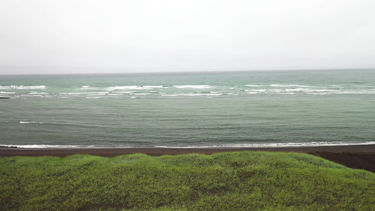 푸른 잔디와 바다가 있는 아이슬란드의 검은 모래 해변과 드론 영상이 위로 올라갑니다