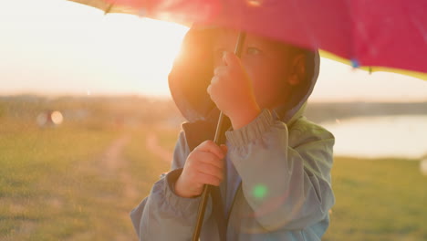 un niño pequeño sosteniendo un paraguas colorido en la lluvia al atardecer