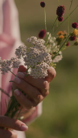 primer plano de un jardinero con una camisa rosa abierta y un polo blanco, arreglando cuidadosamente las flores en las manos, con vibrantes flores rojas, amarillas y blancas contra el fondo de un campo de hierba